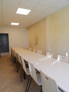 aménagement d'espaces et agencement de mobilier pour le Collegium de Bayeux : table de réunion, chaises empilables, sièges de conférence, canapé lounge, bar central